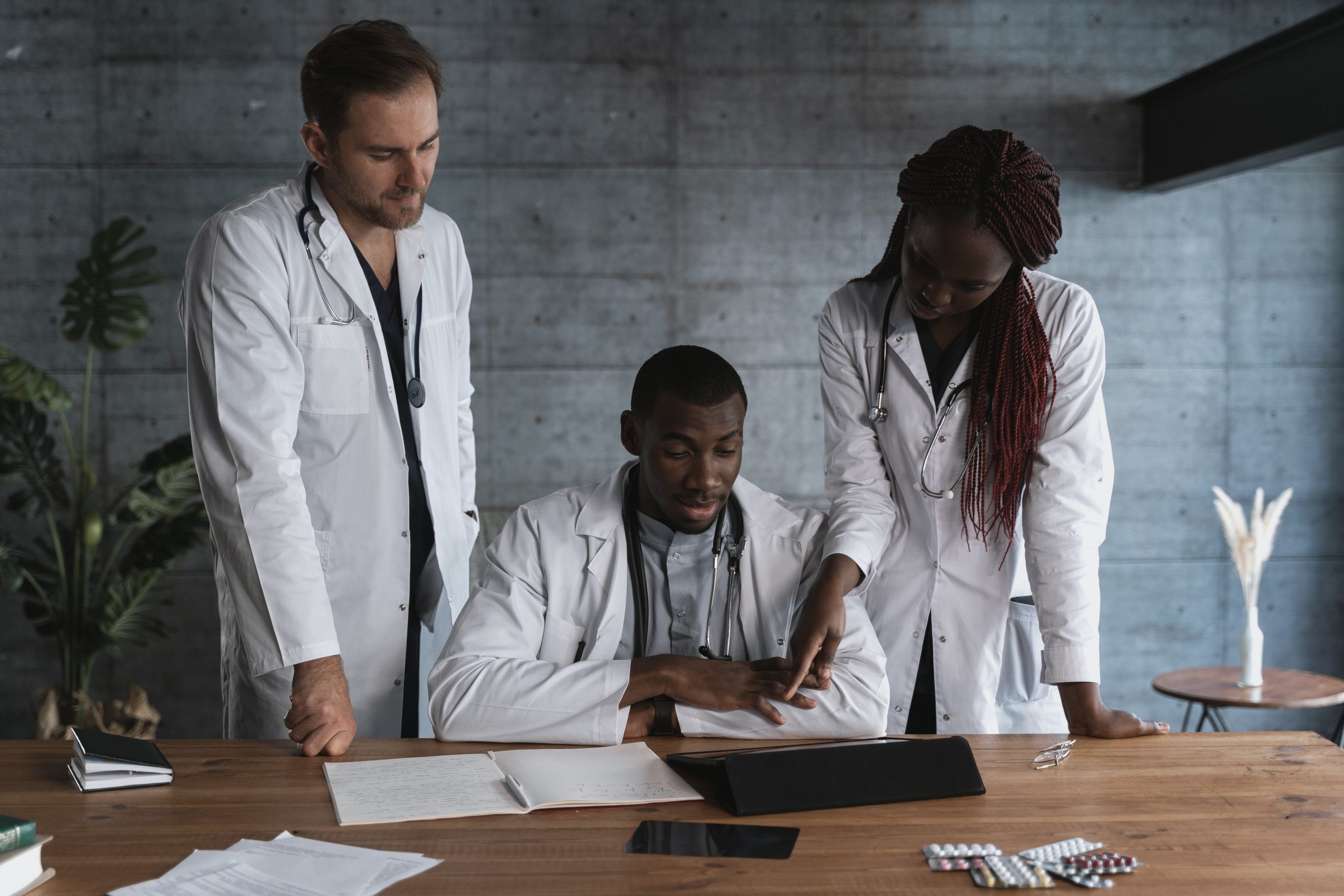 Three healthcare professionals collaborating around a digital tablet while reviewing clinic operations and growth strategies, representing medical cybersecurity financing, urgent care center funding, neighborhood health center financing, patient portal financing, and patient billing cash flow financing for modern healthcare organizations.