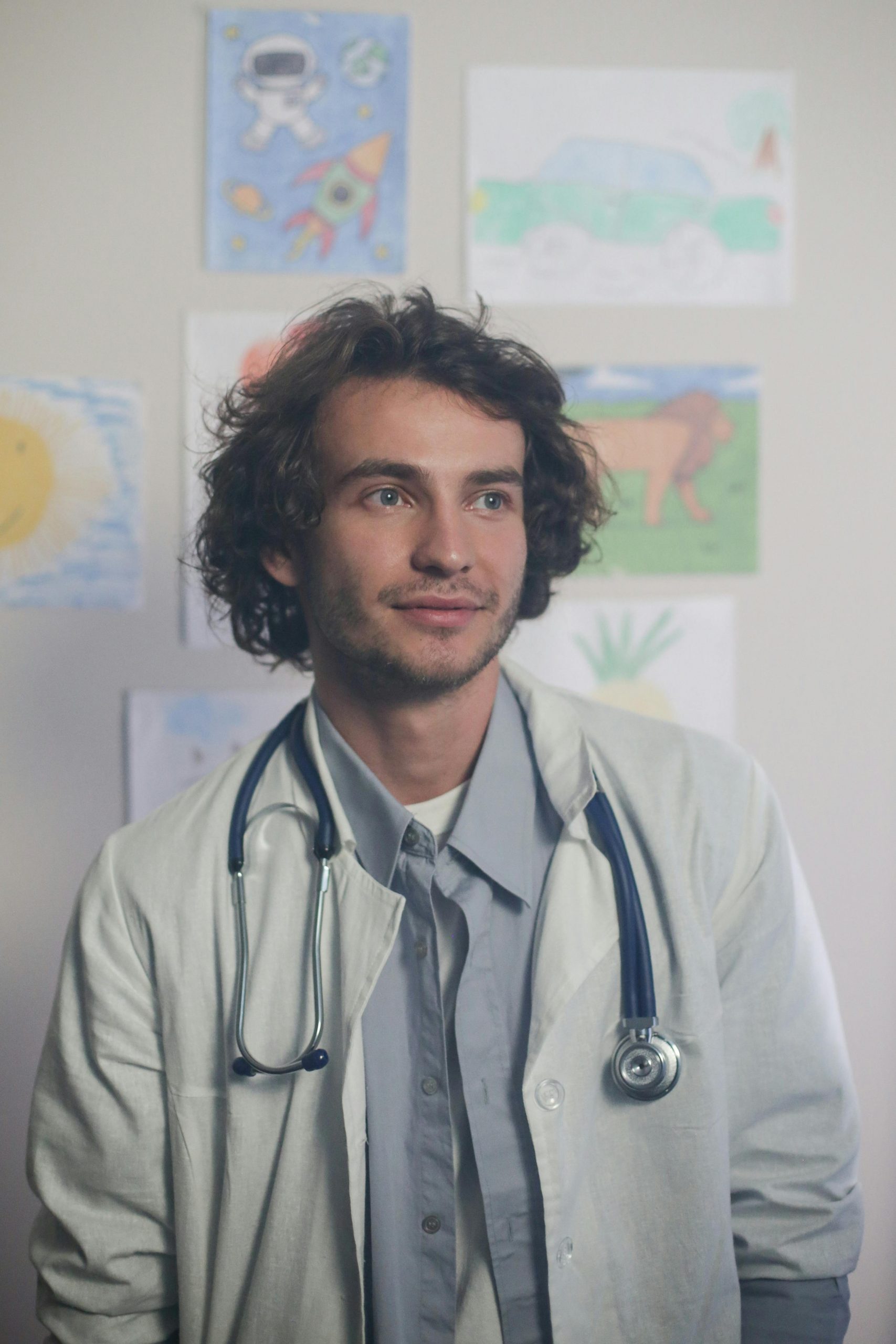 Family physician standing in a pediatric healthcare setting with children's artwork displayed in the background, representing healthcare organizations seeking family medicine clinic funding, funding for medical practices, physician acquisition financing, nonprofit hospital financing, and tax exempt hospital financing to expand services, acquire practices, improve facilities, and strengthen community healthcare access.
