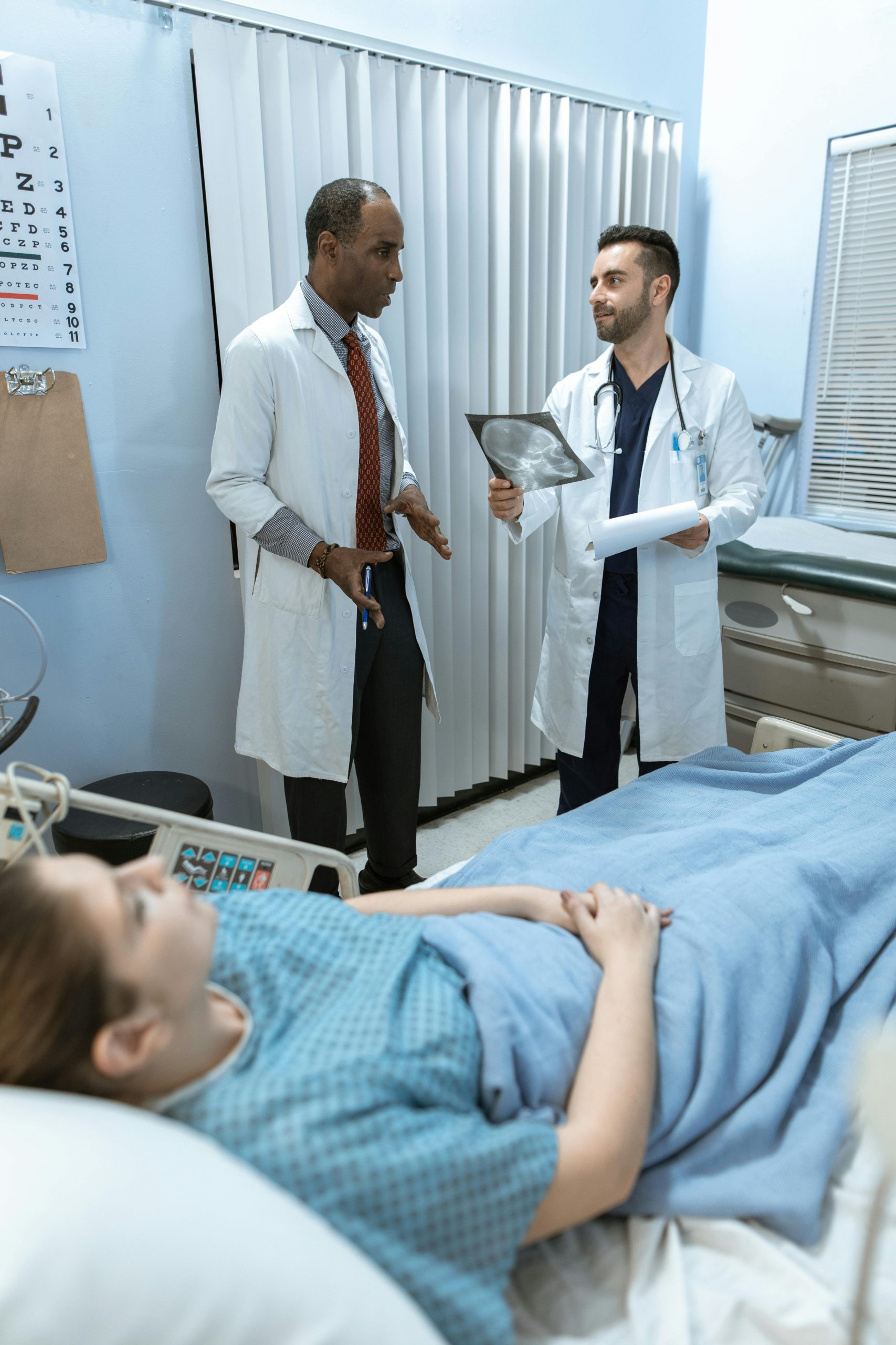 Doctors reviewing patient imaging and discussing treatment plans at a hospital bedside while a patient receives care, representing public hospital financing, clinic tenant improvement financing, medical practice scaling capital, and hospital funding used to expand healthcare services, renovate facilities, and improve patient care delivery.