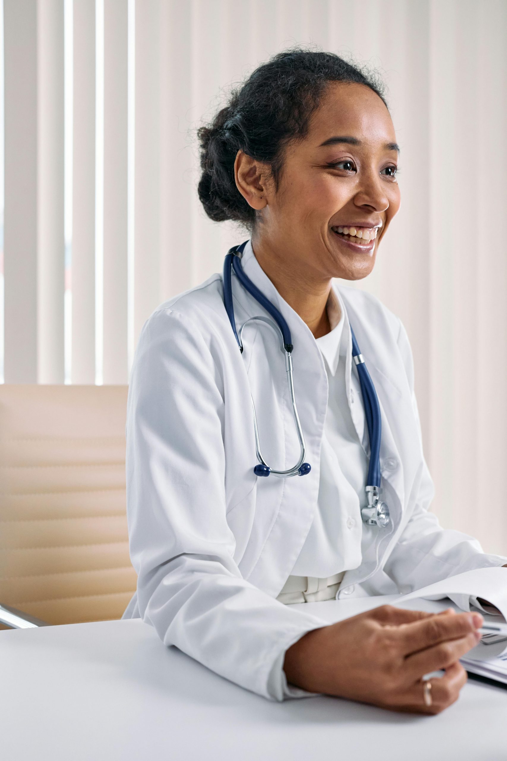 Smiling physician seated in a modern medical office reviewing patient information, representing Physician Office Financing, medical office building loans, medical practice equipment financing, internal medicine practice financing, and physician practice loans used to start, expand, or modernize healthcare practices.